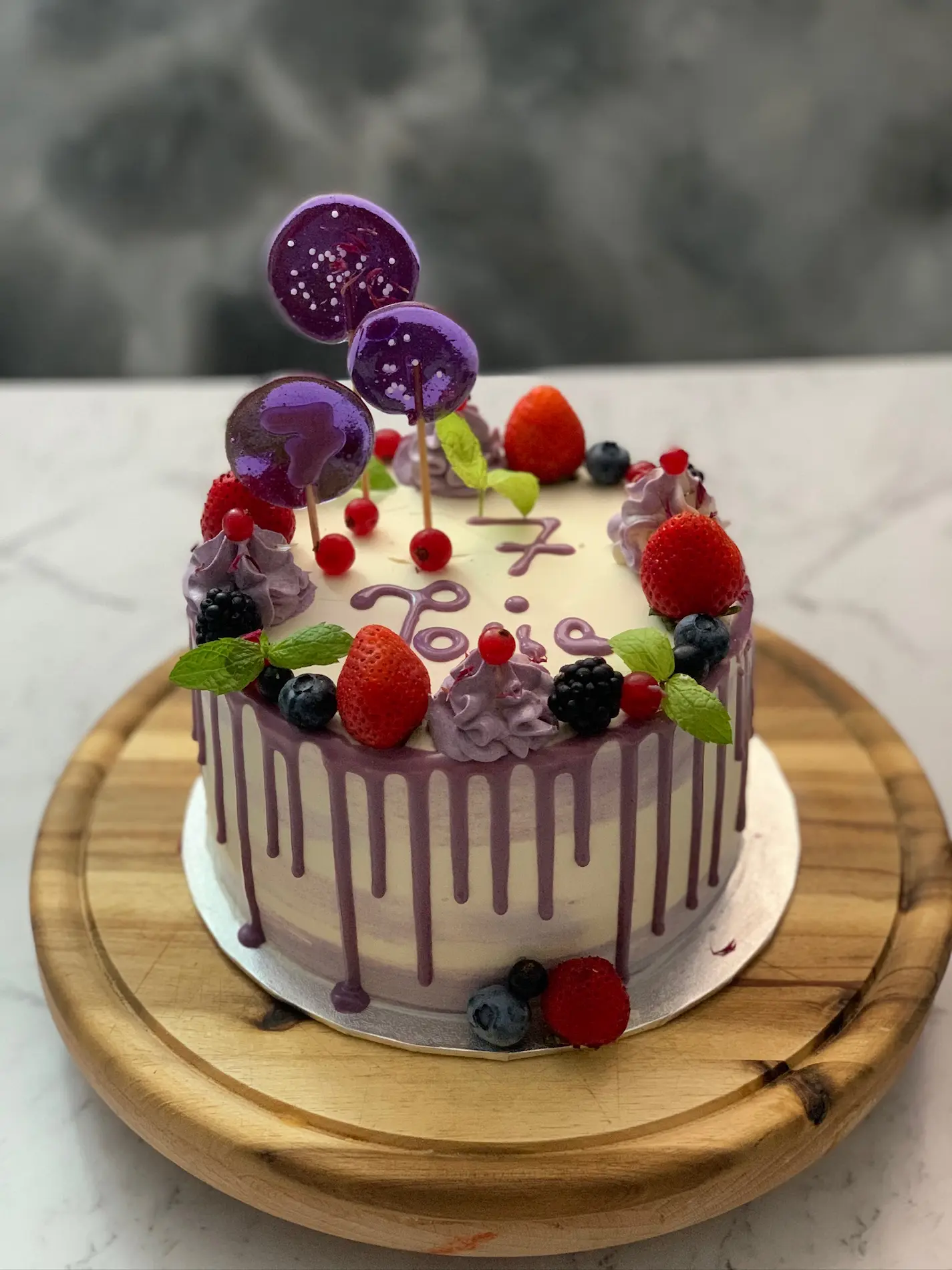 Tort dziecięcy drip cake z fioletową polewą, świeżymi owocami i cukrowymi lizakami