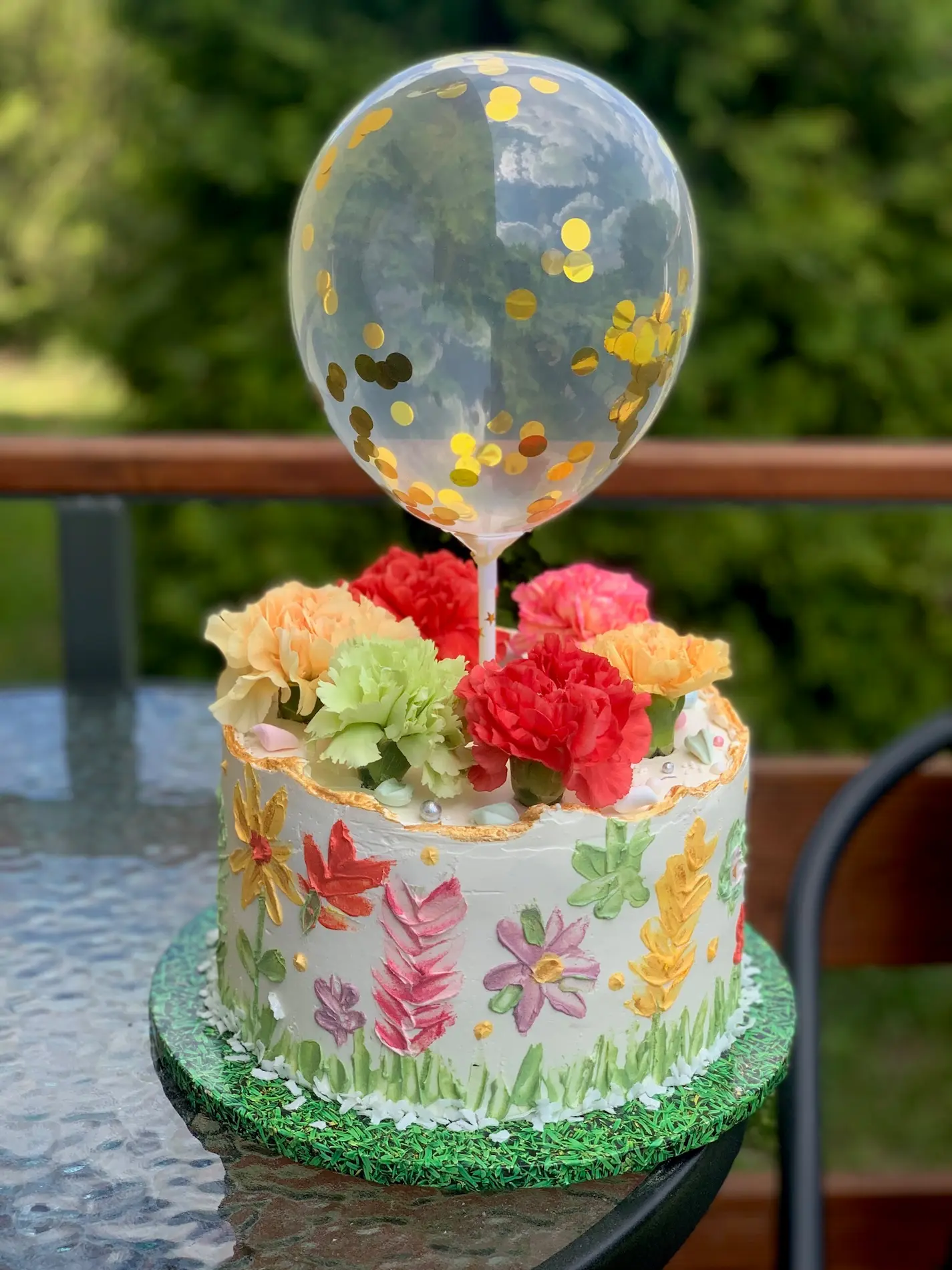 Tort dziecięcy z motywem łąki kwiatowej, kolorowymi goździkami i balonem ze złotym konfetti