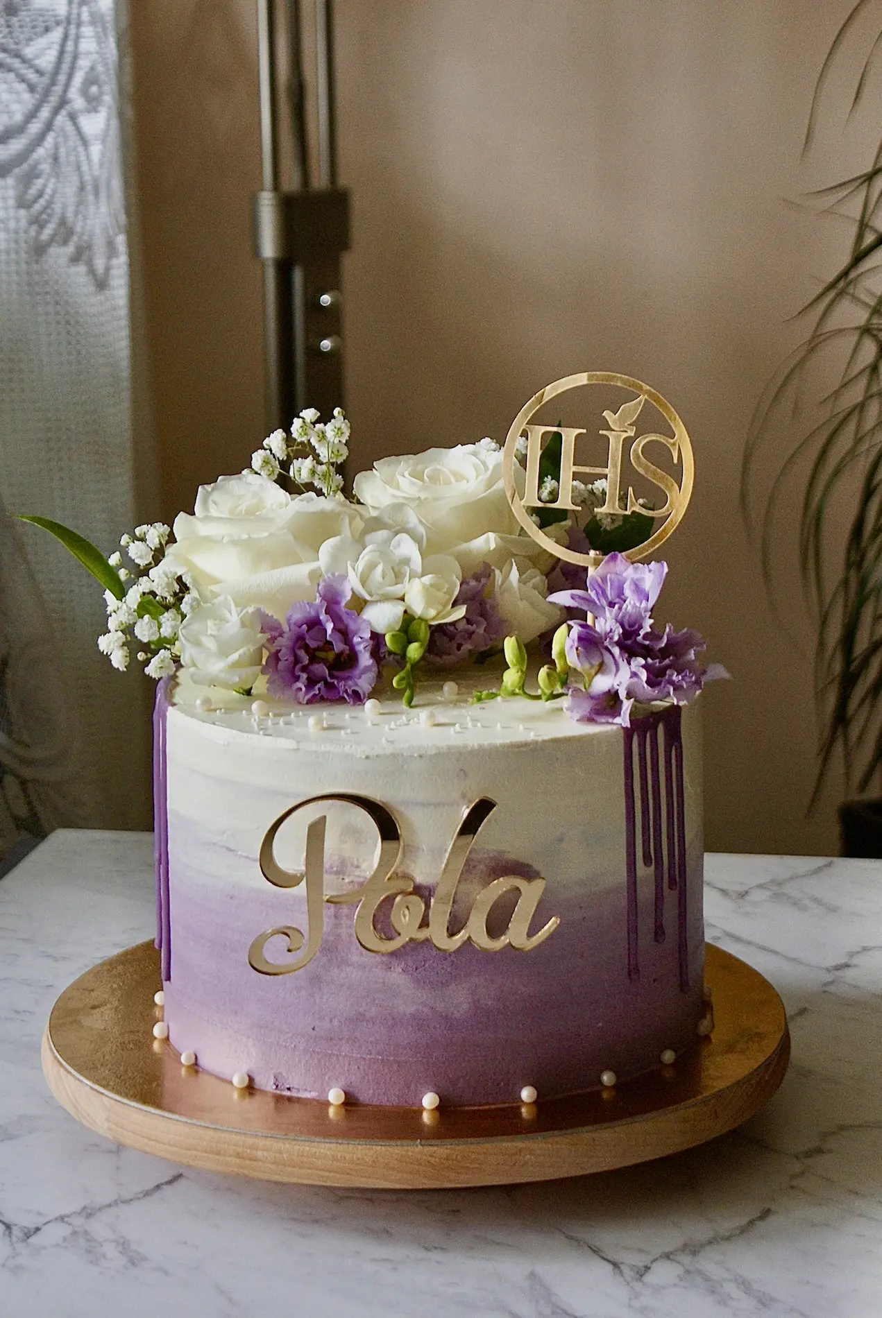 Tort komunijny z fioletowym gradientem, personalizowanym imieniem Pola, symbolem IHS i świeżymi kwiatami