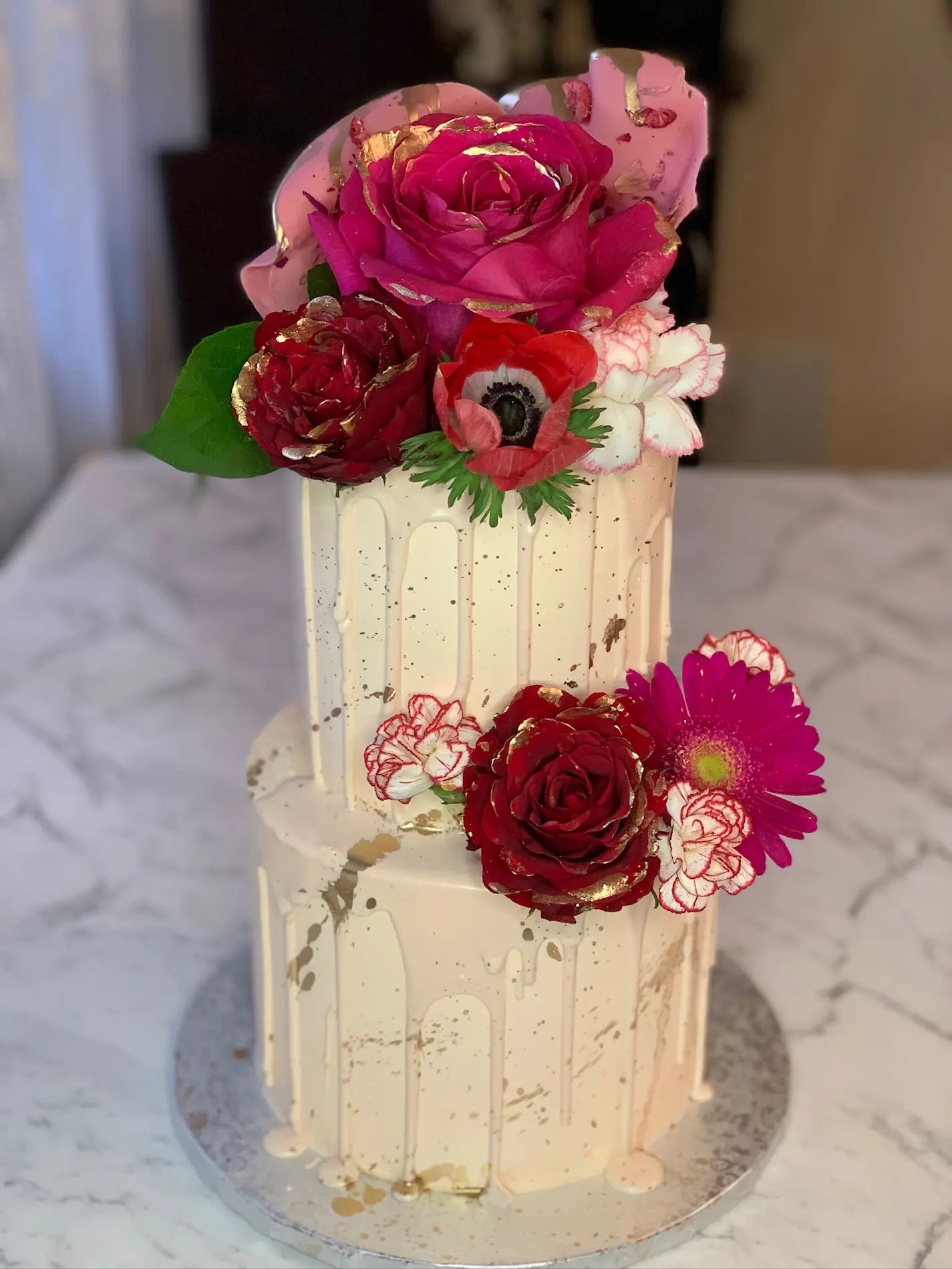 Dwupiętrowy tort biały drip cake ze świeżymi czerwonymi różami, anemonami i złotymi akcentami