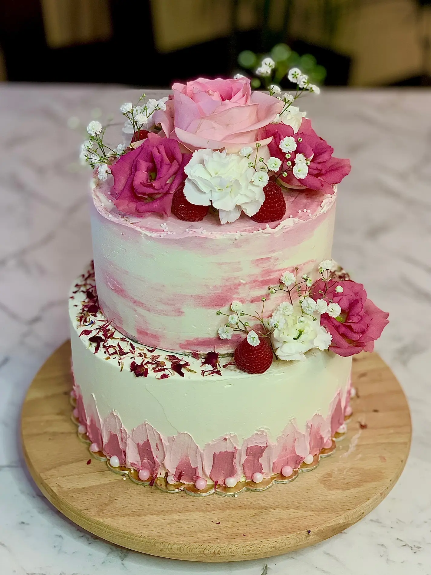 Dwupiętrowy tort z różowo-białym gradientem, świeżymi kwiatami, truskawkami i listkami herbaty