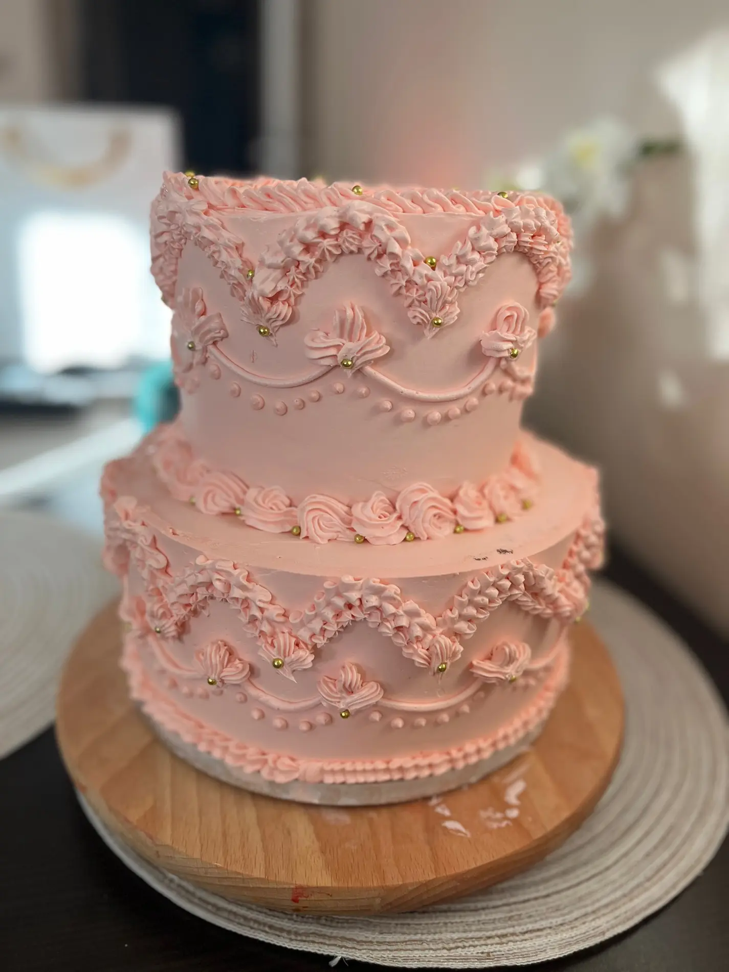 Dwupiętrowy tort różowy w stylu vintage z koronkowymi zdobieniami z kremu i złotymi perełkami
